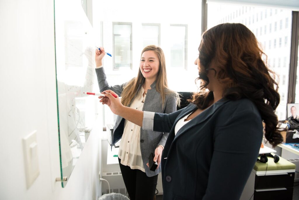 Two women discussing next to a dry-erase board in an office